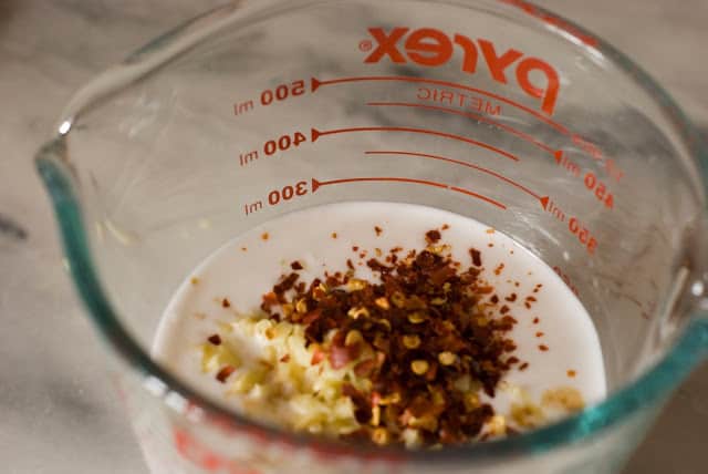 measuring cup with coconut milk, fresh ginger, and red pepper flakes