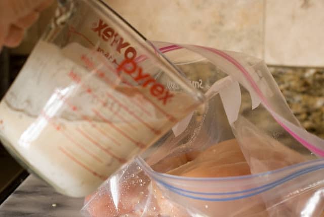 plastic bag with chicken breasts pouring coconut milk marinade over
