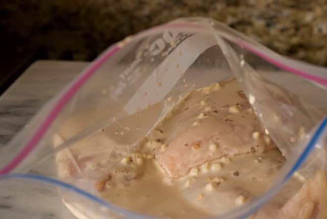 plastic bag with chicken breasts pouring coconut milk marinade over