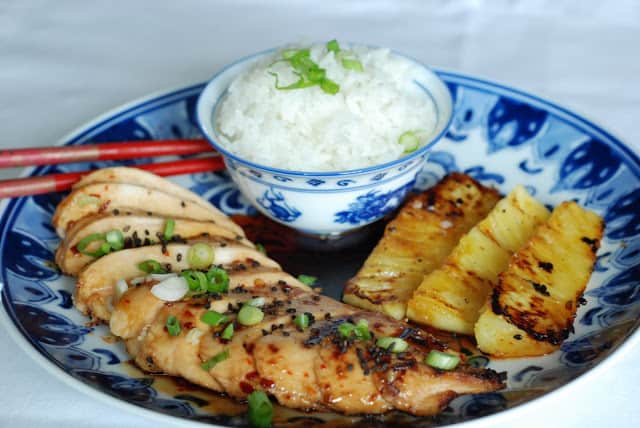 Sliced grill chicken breast with rice and grilled pineapple on blue and white plate