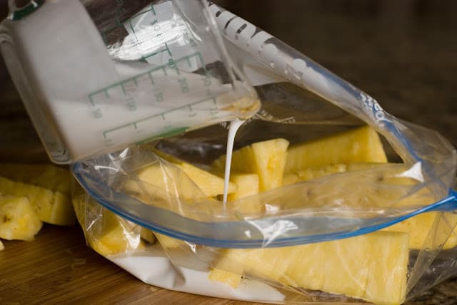 Fresh pineapple slices in resealable bag with coconut milk being poured into bag