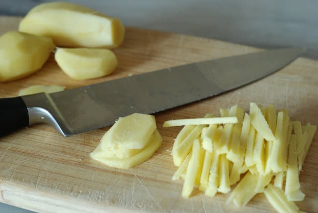 fresh ginger slices julienned on wood board with butcher knife