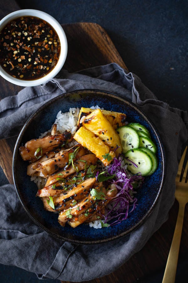 Blue bowl with rice topped with sliced coconut sticky chicken with grilled pineapple