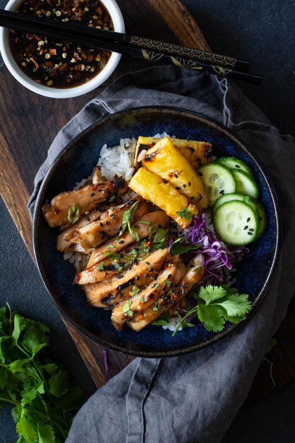 blue bowl on wooden board with white rice topped with sticky coconut chicken with grilled pineapple