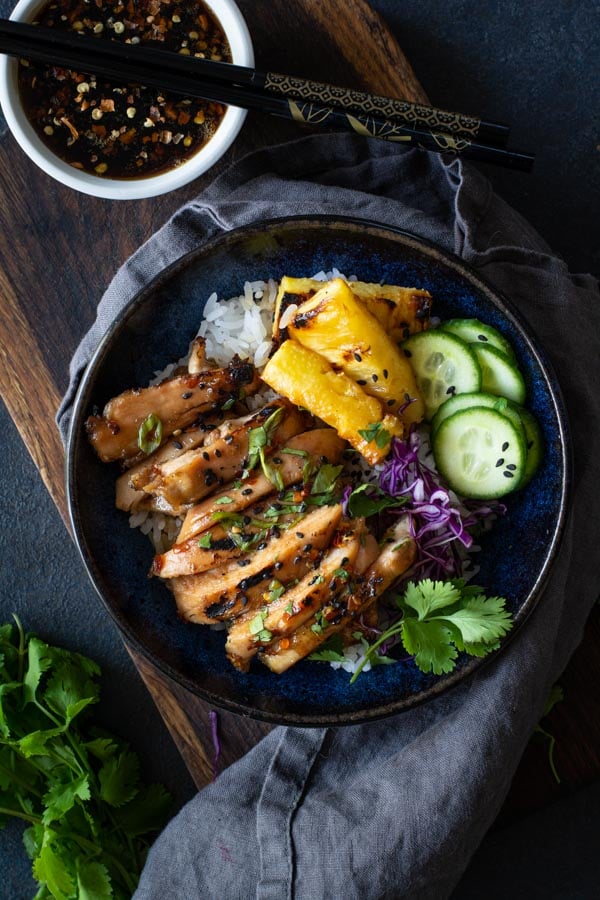 blue bowl on wooden board with white rice topped with coconut sticky chicken with grilled pineapple