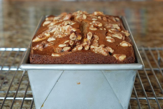 Baked banana nut bread in pan sitting on a cooling rack.
