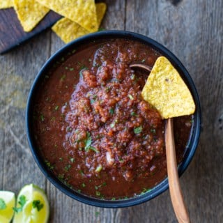Bowl of fire roasted salsa with a tortilla chip on top. Side of limes and more tortillas.