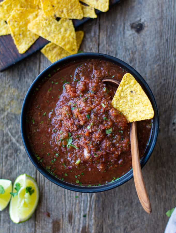 Bowl of fire roasted salsa with a tortilla chip on top. Side of limes and more tortillas.