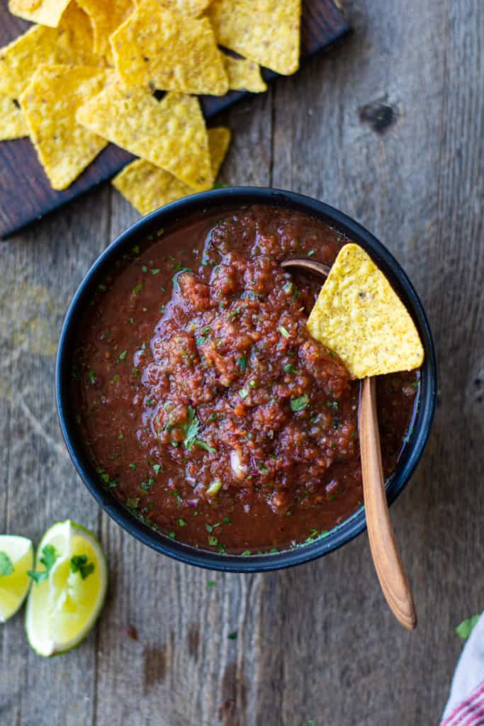Bowl of fire roasted canned tomato salsa with a tortilla chip on top. Side of limes and more tortillas.