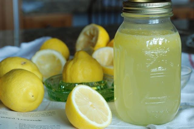 Many cut lemons surrounding a quart jar filled with lemonade syrup
