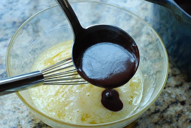 Ladle pouring in chocolate mixture into egg sugar mixture