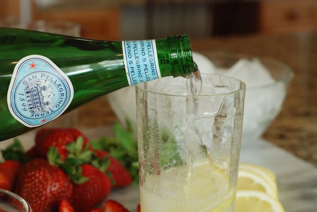 Sparkling water pouring into a tall glass of lemonade syrup