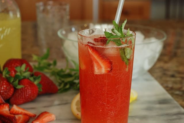 Tall glass of strawberry old fashioned lemonade with fresh strawberries and a sprig of mint