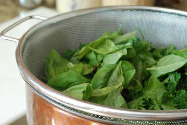 strainer of fresh basil and parsley sat in pot of boiling water