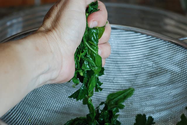 Hand squeezing water our of blanched basil and parsley