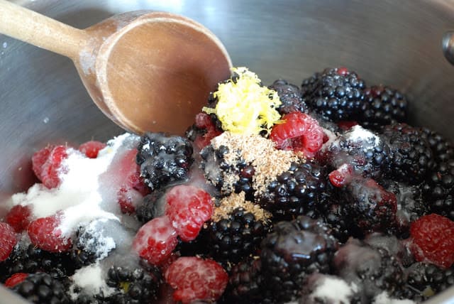 berries, sugar, lemon zest, nutmeg, being stirred together in sauce pan with wooden spoon