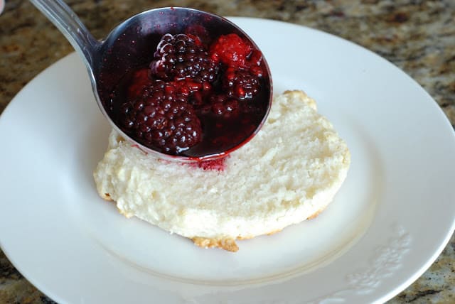 bottom half of biscuit on a white plate with a ladle of berries mixture