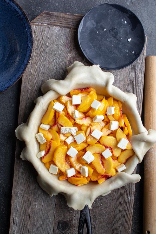 Sliced peaches on top of pie dough dotted with butter