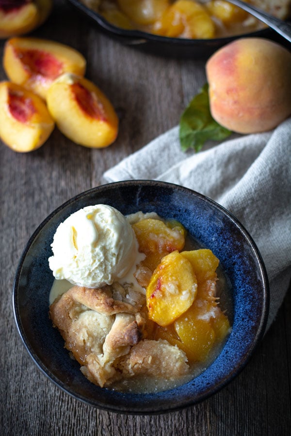 Southern peach cobbler spooned into bowl topped with vanilla ice cream