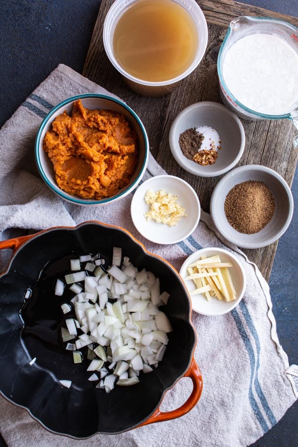 Pot with chopped onions surrounded by bowls of pumpkin and spices