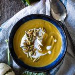 blue bowl with pumpkin soup, drizzle of coconut milk and toasted pumpkin seeds