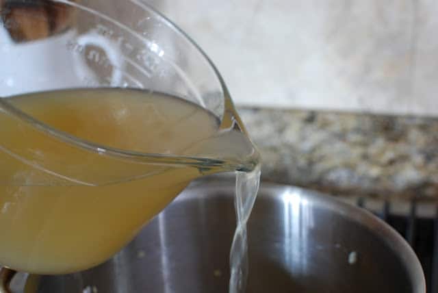 Large measuring cup pouring chicken stock into pot