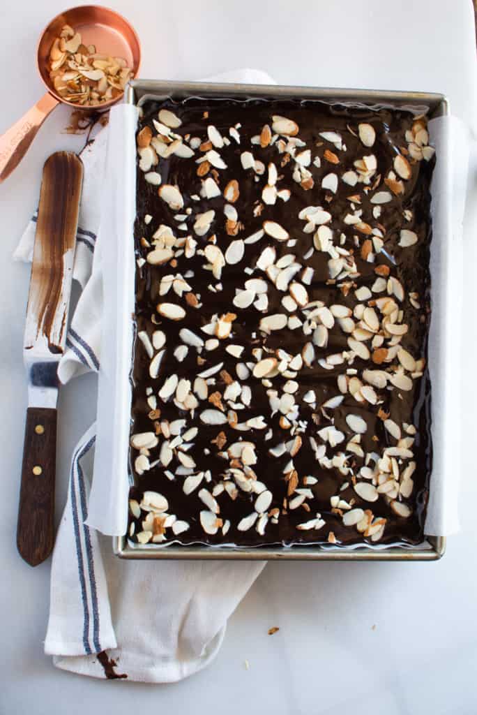 Rectangular pan of baked brownies with chocolate ganache spread on top and sprinkled sliced almonds.