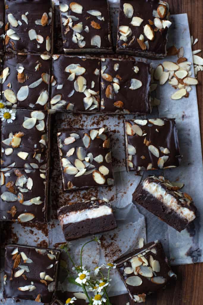 Cut up squares of Coconut Fudge Brownies on a wooden board with side view of sliced brownies.