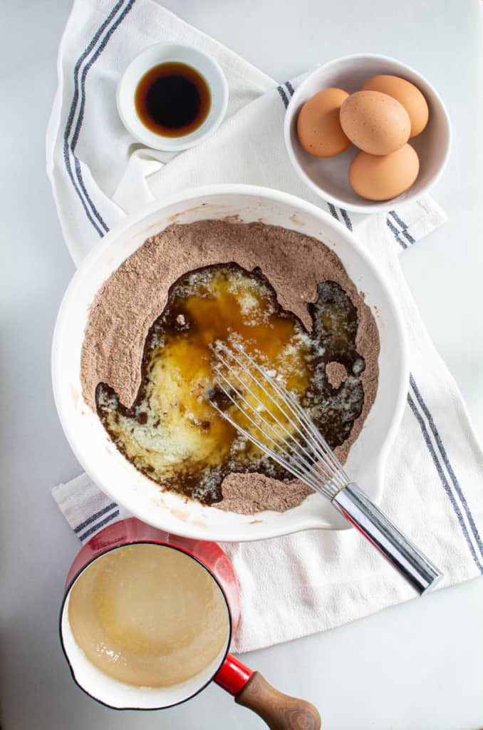Bowl with mixed sugar, flour, cocoa powder, and melted butter and whisk for mixing. Bowl with eggs and vanilla.