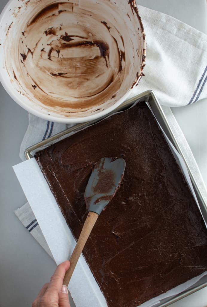 Rectangular pan (9 x 13-inch) with brown batter spooned and smoothed on top. Empty brownie batter bowl .