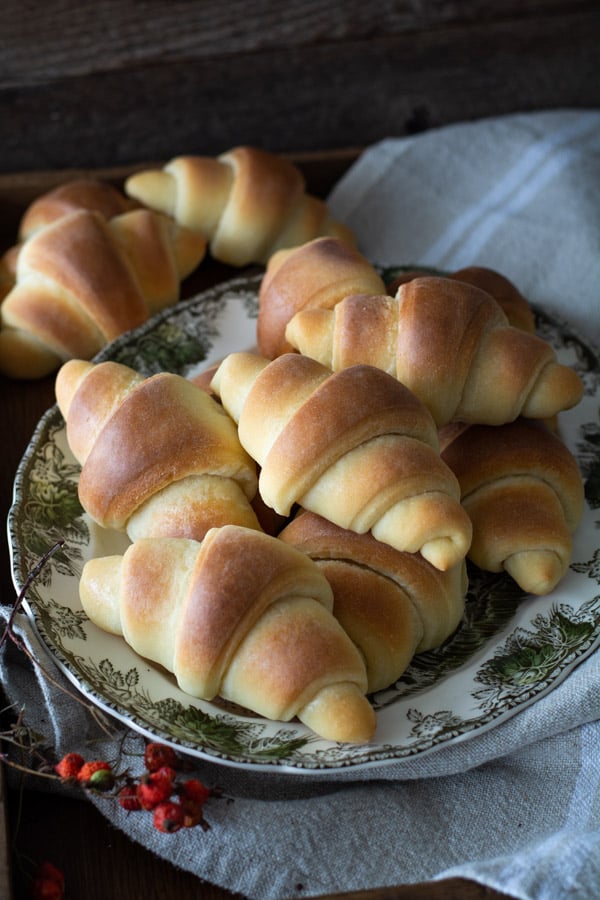 Baked crescent dinner rolls on a platter with linen cloth.