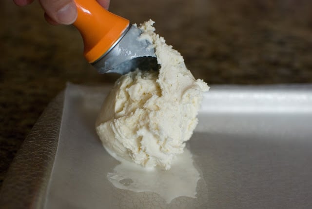 Scoop with balls of vanilla frozen dessert treat dropping onto a baking sheet.