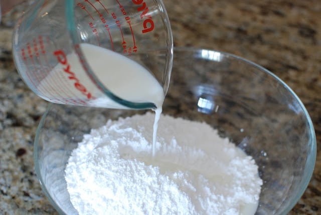 measuring cup with milk pouring into powdered sugar