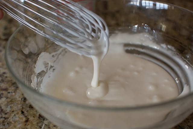 Icing glaze drizzling from wire whisk