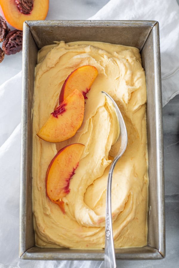 Overhead shot of peach ice cream in a metal pan with silver spoon