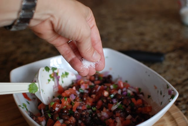 hand sprinkling salt over black bean salsa