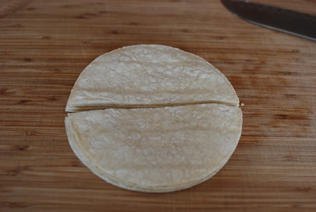 Corn tortillas cut in half on a cutting board