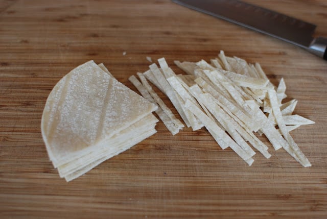Corn tortillas cut into strips on a cutting board