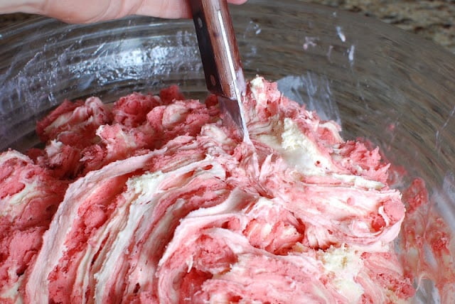 Raspberry sorbet and vanilla ice cream being blended in a bowl.