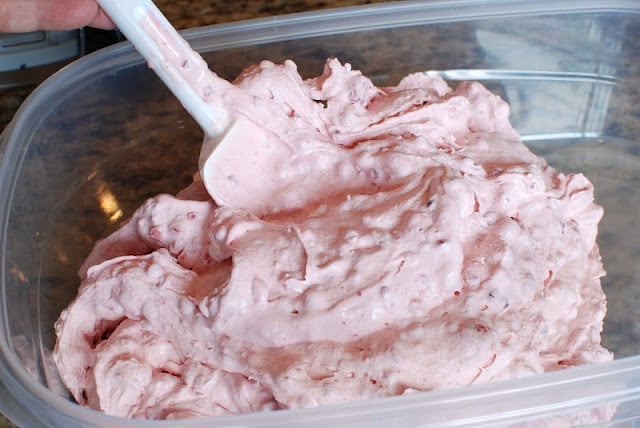 Spatula running through container of homemade pink strawberry raspberry ice cream.