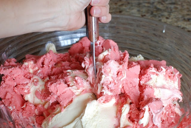 Hand mixing ice cream in a bowl with metal spoon.