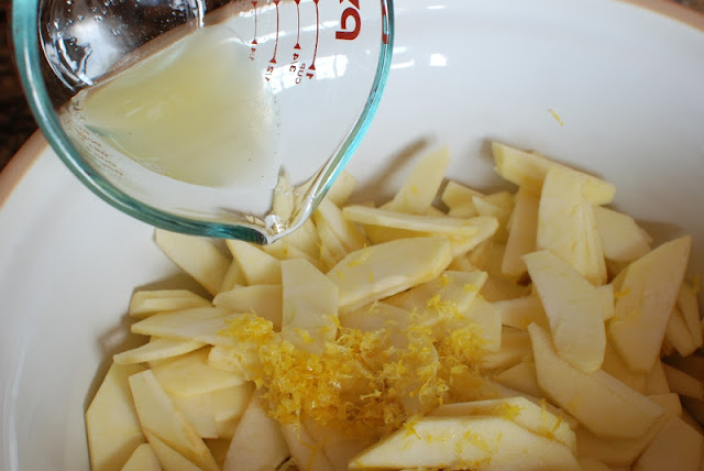 Large bowl with thin slices of apples, lemon zest, and lemon juice pouring into the bowl