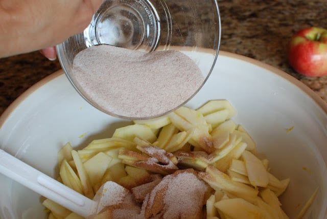 Cinnamon and sugar sprinkled over top of slice apples in a large bowl.