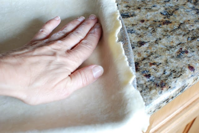 A hand pressing the pastry dough into a baking sheet.