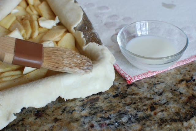 Pastry brush with milk brushed around edges of pie crust.