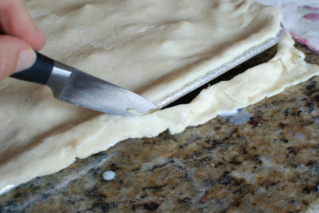 Paring knife cutting off the excess pie dough from around the edges of the pan.