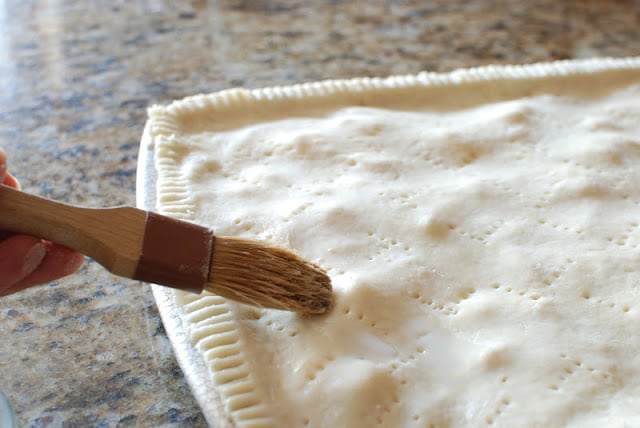 Pastry brush topping pie crust with milk.
