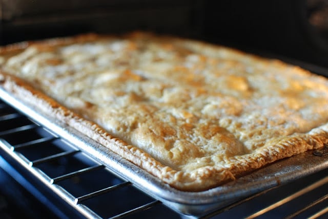 Golden baked slab apple pie removing from oven.