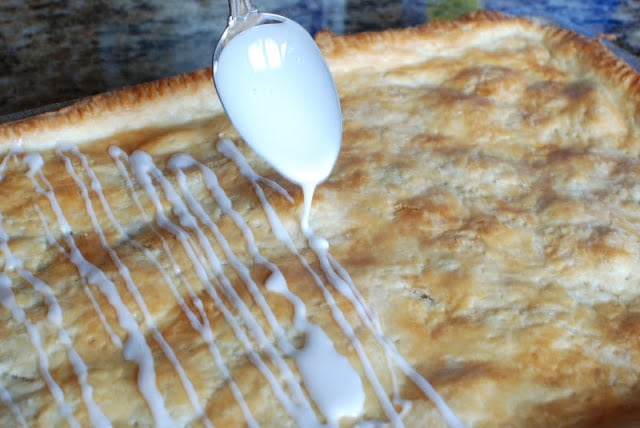 Spoon drizzling glaze over top of the slab apple pie