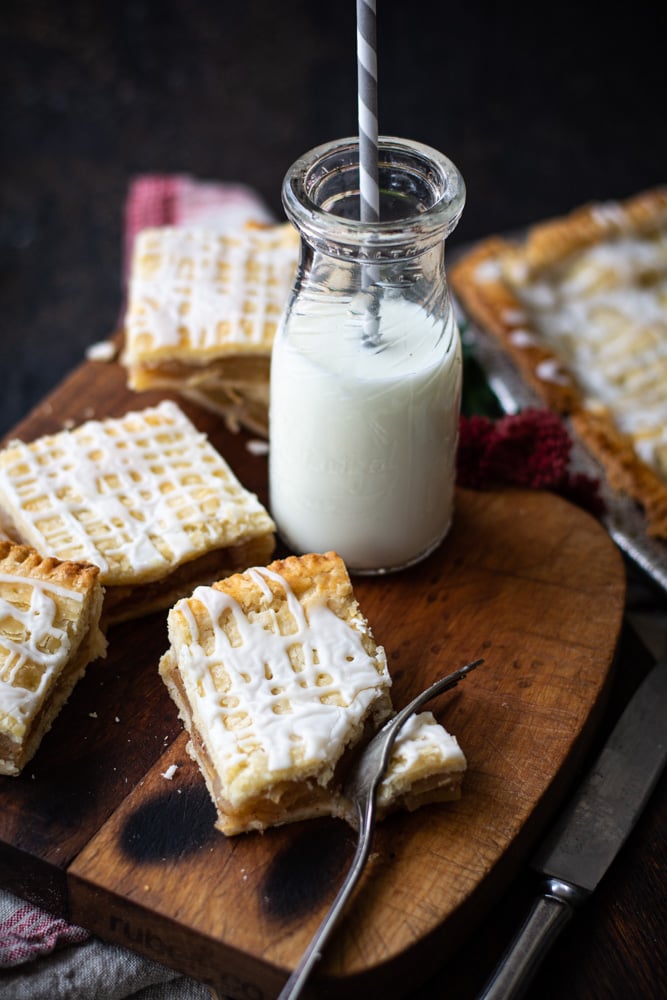 Slab apple pie squares on top of a cutting board with a bottle of milk.